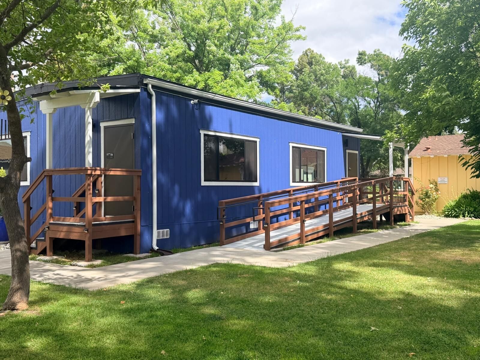 A blue mobile home with a wooden porch and a ramp.