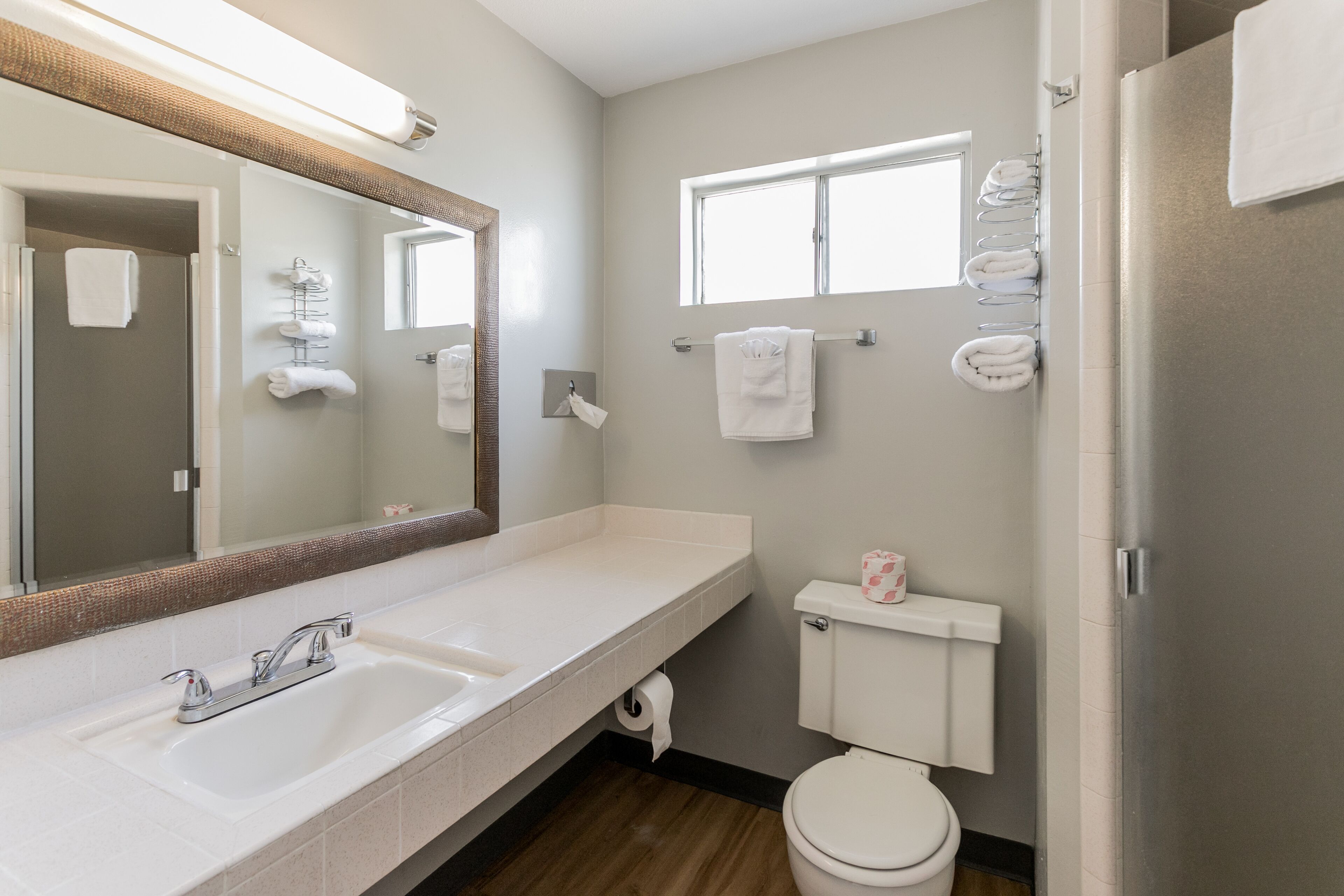 A modern bathroom with a double sink, a large mirror, a toilet, and a window.