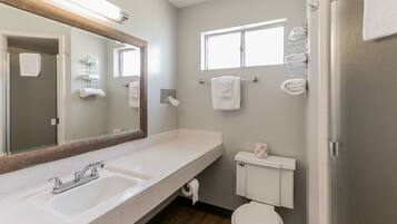 A modern bathroom with a double sink, a large mirror, a toilet, and a window.