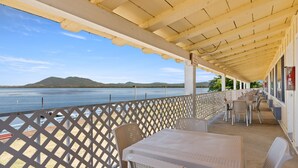 A covered outdoor seating area with tables and chairs, overlooking a body of water and distant mountains.