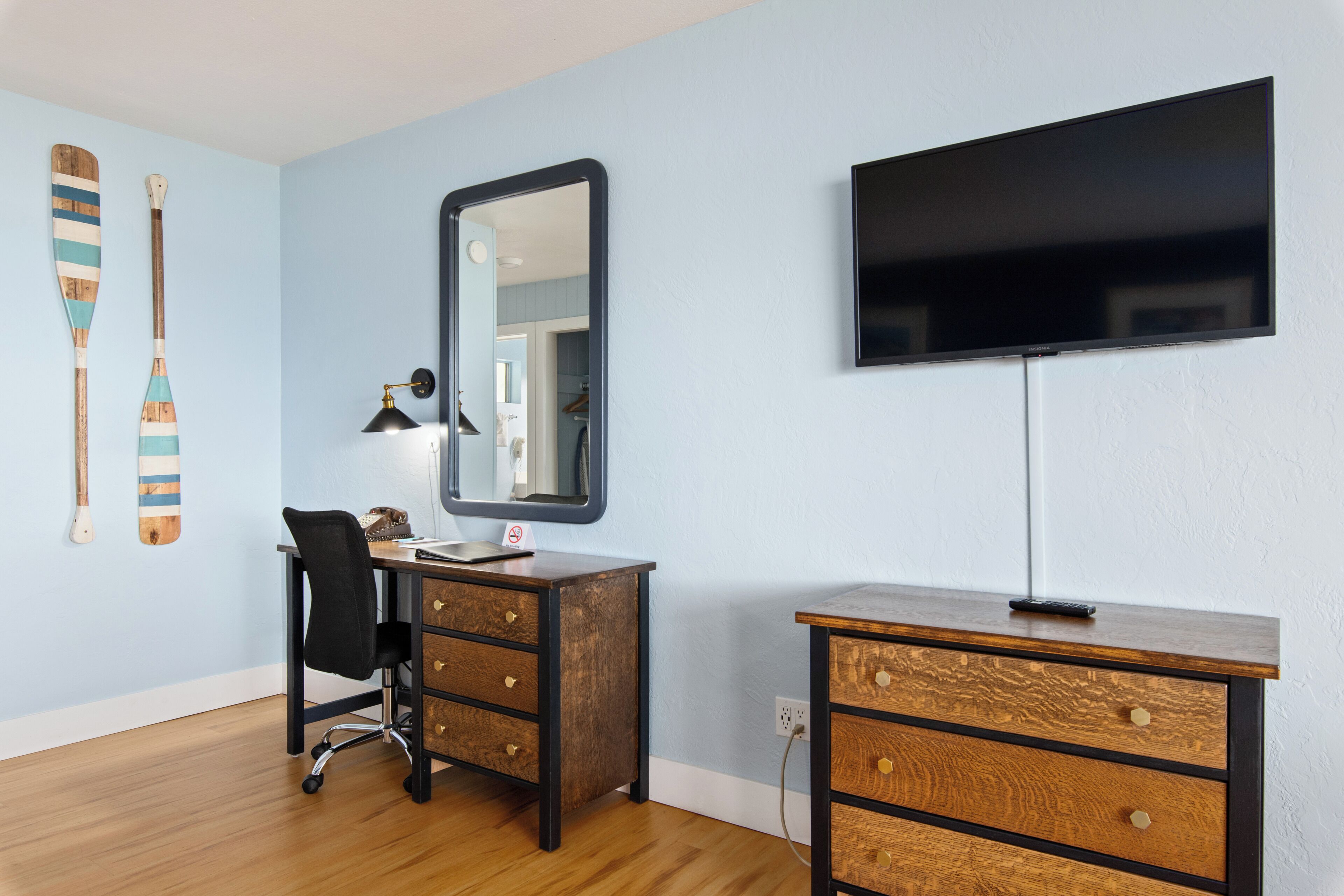 Habitación con escritorio, silla, espejo, televisor y detalles decorativos de madera en la pared.