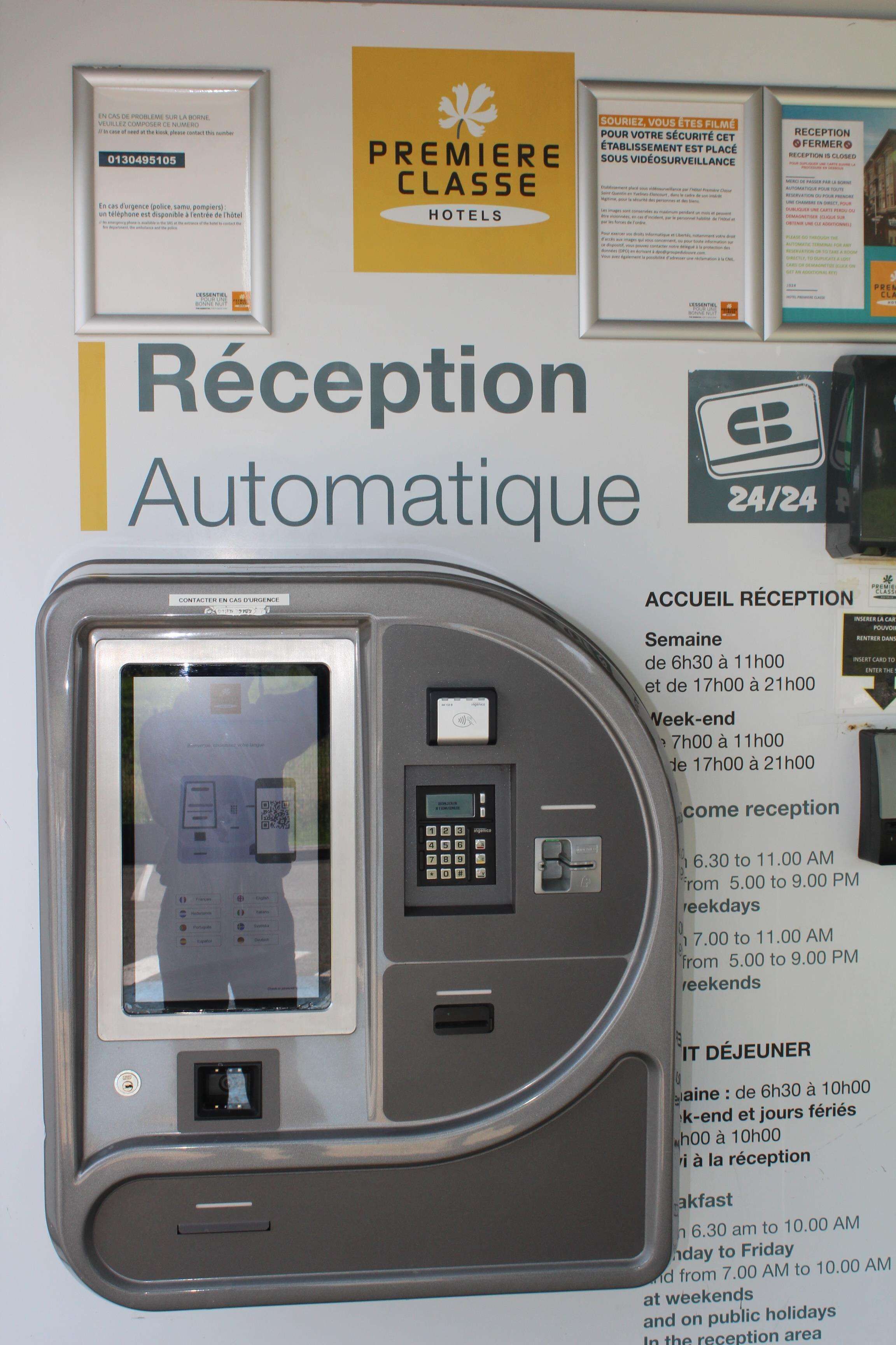 Un quiosco de recepción con una pantalla y teclado, rodeado de carteles informativos y un letrero que dice 'RÉCEPTION AUTOMATIQUE'.