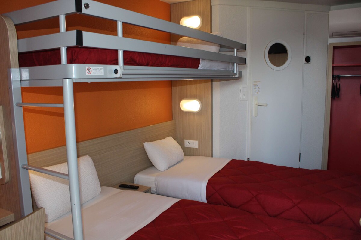 Habitación con literas, una puerta y una lámpara fijada a la pared.