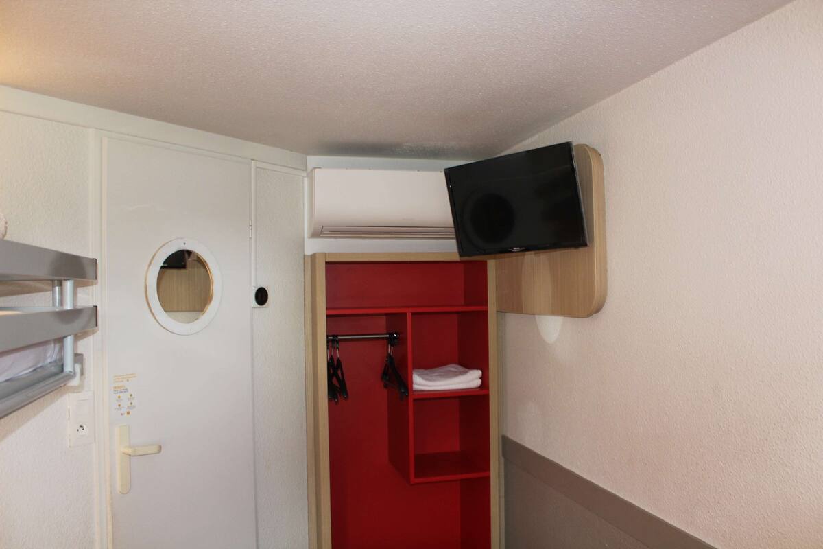 A compact room with a white door, a red storage unit, and a mounted black speaker.
