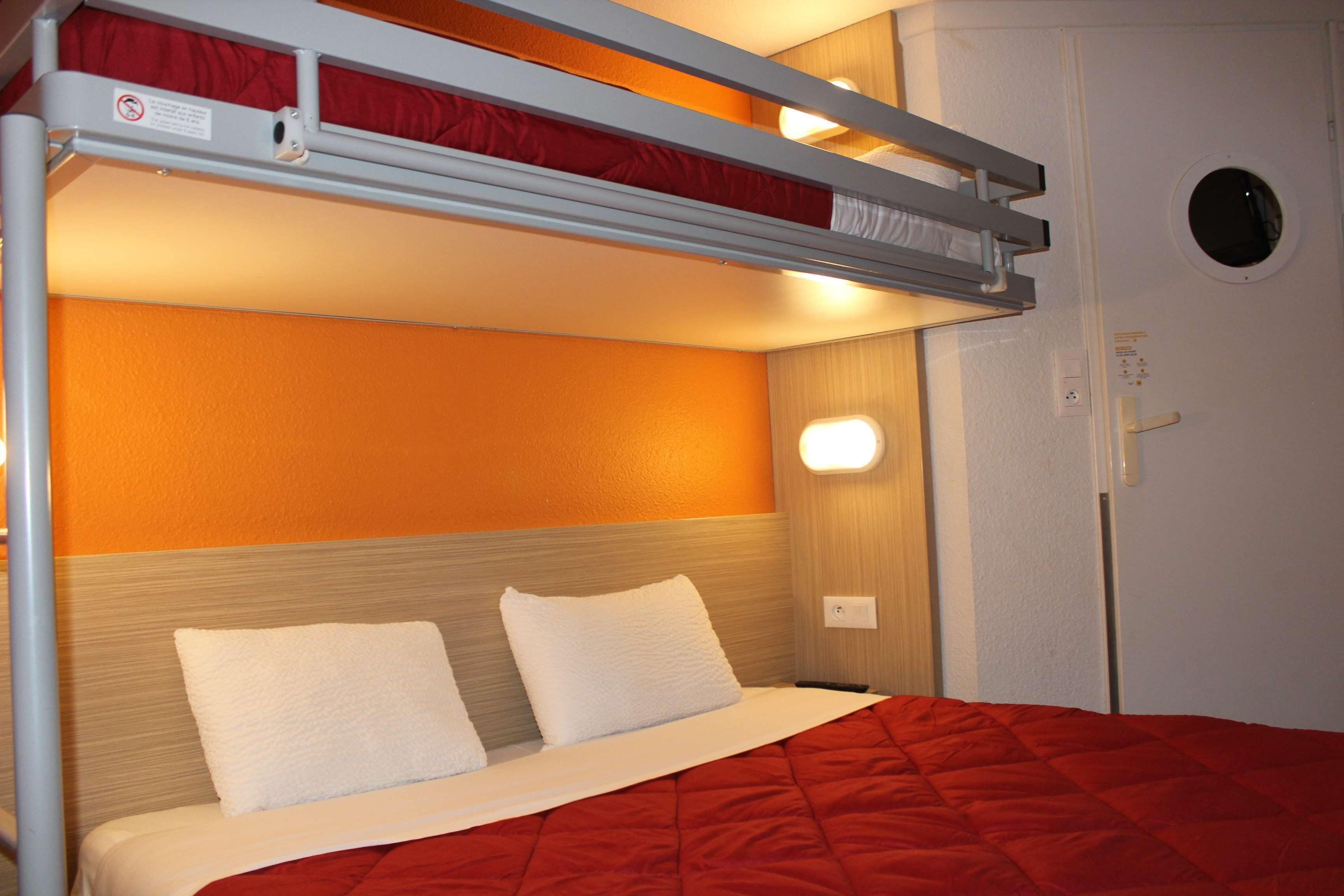 A bunk bed with a red quilt, white pillows, and a wooden headboard.