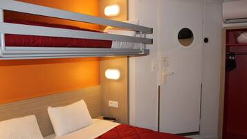A bunk bed with white bedding, a red quilt, and a white pillow. There is a white wardrobe with a circular window and a door handle.