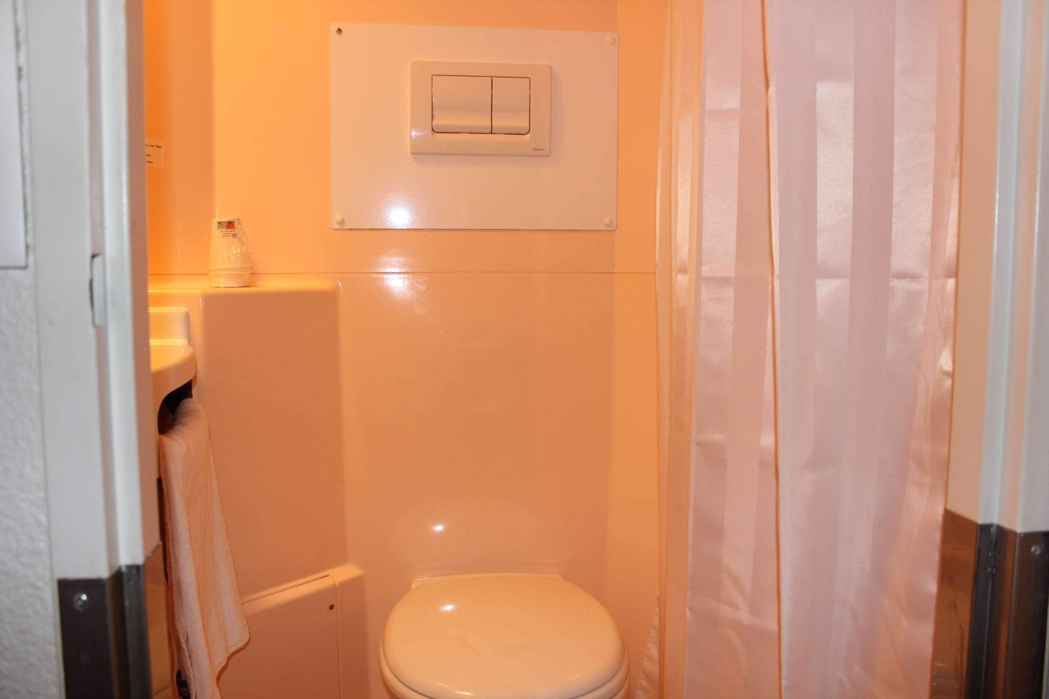 A small, compact bathroom with a toilet, a towel rack, and a wall-mounted light switch.