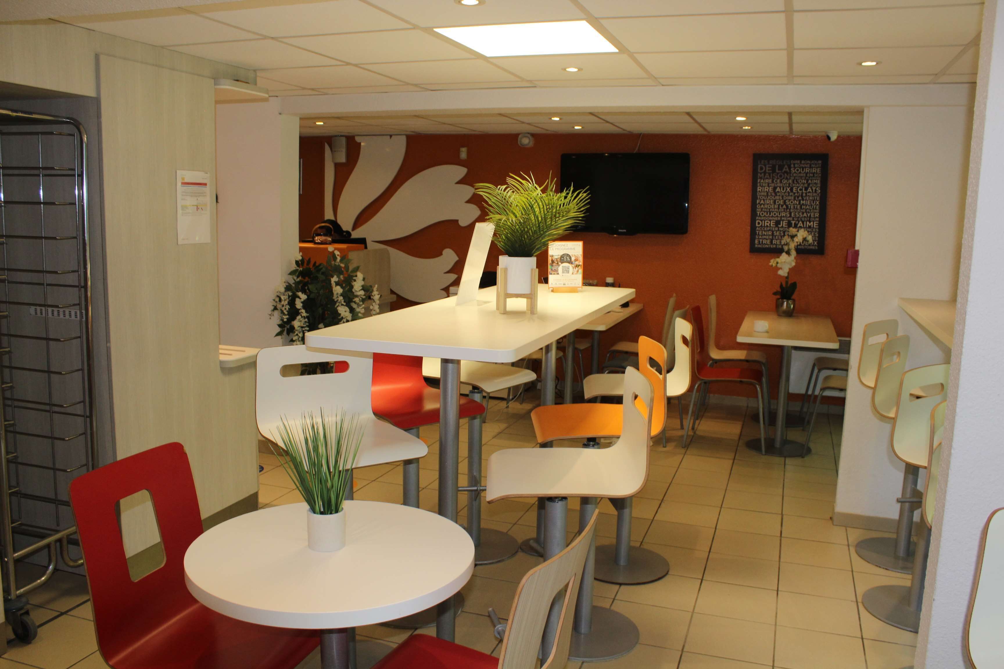 A modern restaurant with round tables and red chairs, featuring a potted plant on each table.