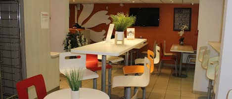 A modern restaurant with round tables and red chairs, featuring a potted plant on each table.