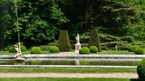 Un jardín formal con una fuente, setos bien recortados y estatuas.