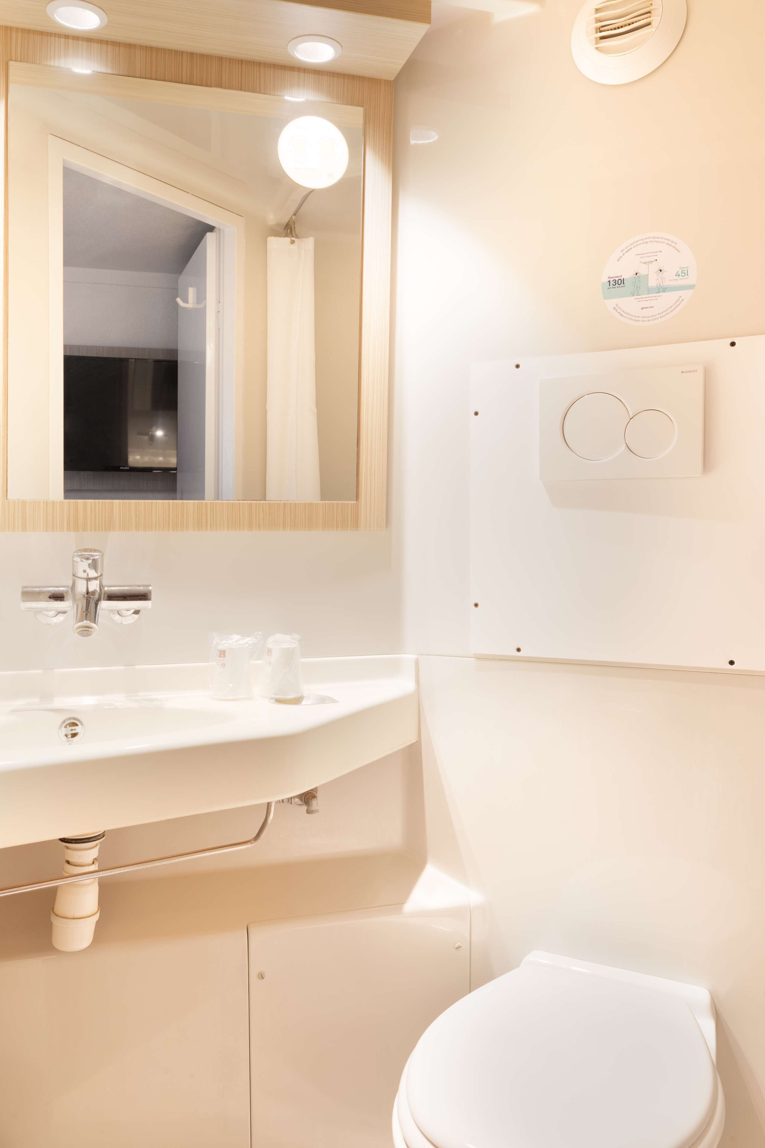 Un baño moderno con lavamanos, espejo y retrete blancos.