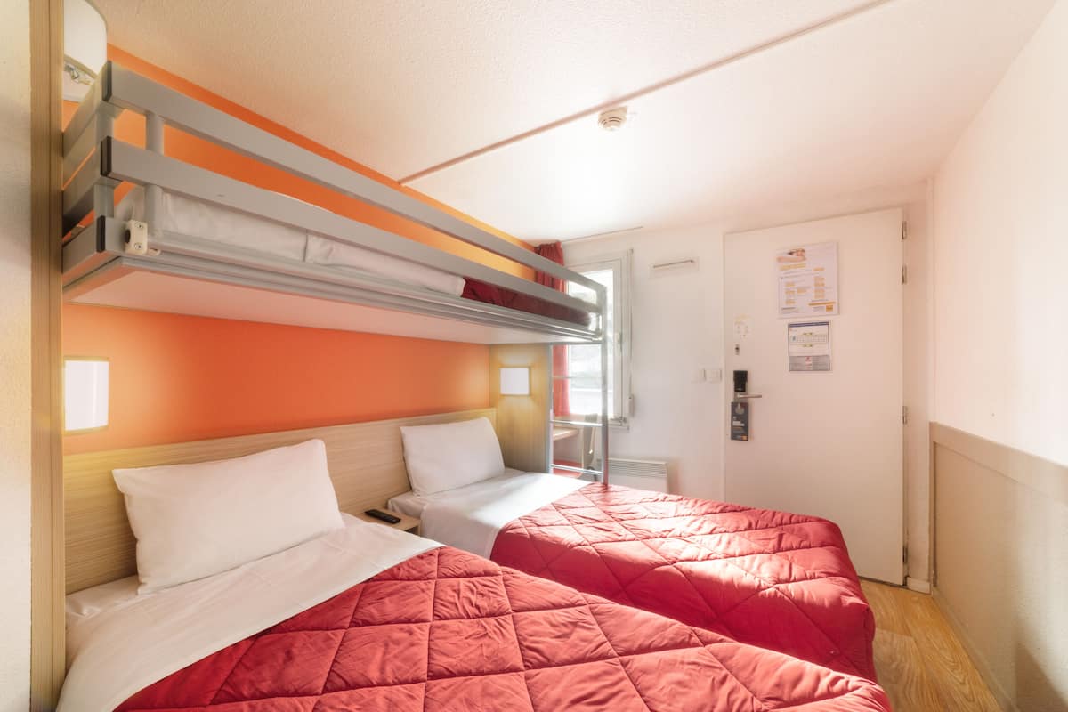 A hotel room with two beds, a bunk bed, a door with a sign, and a window.