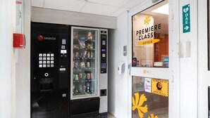 A hotel entrance with a vending machine, a glass door with a yellow leaf decal, and a sign for 'Premiere Classe Hotels'. - Premiere Classe Meaux - Nanteuil les Meaux (Nanteuil-les-Meaux)