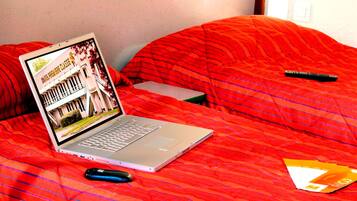 A laptop on a bed with a red blanket, a remote control, and a folder.