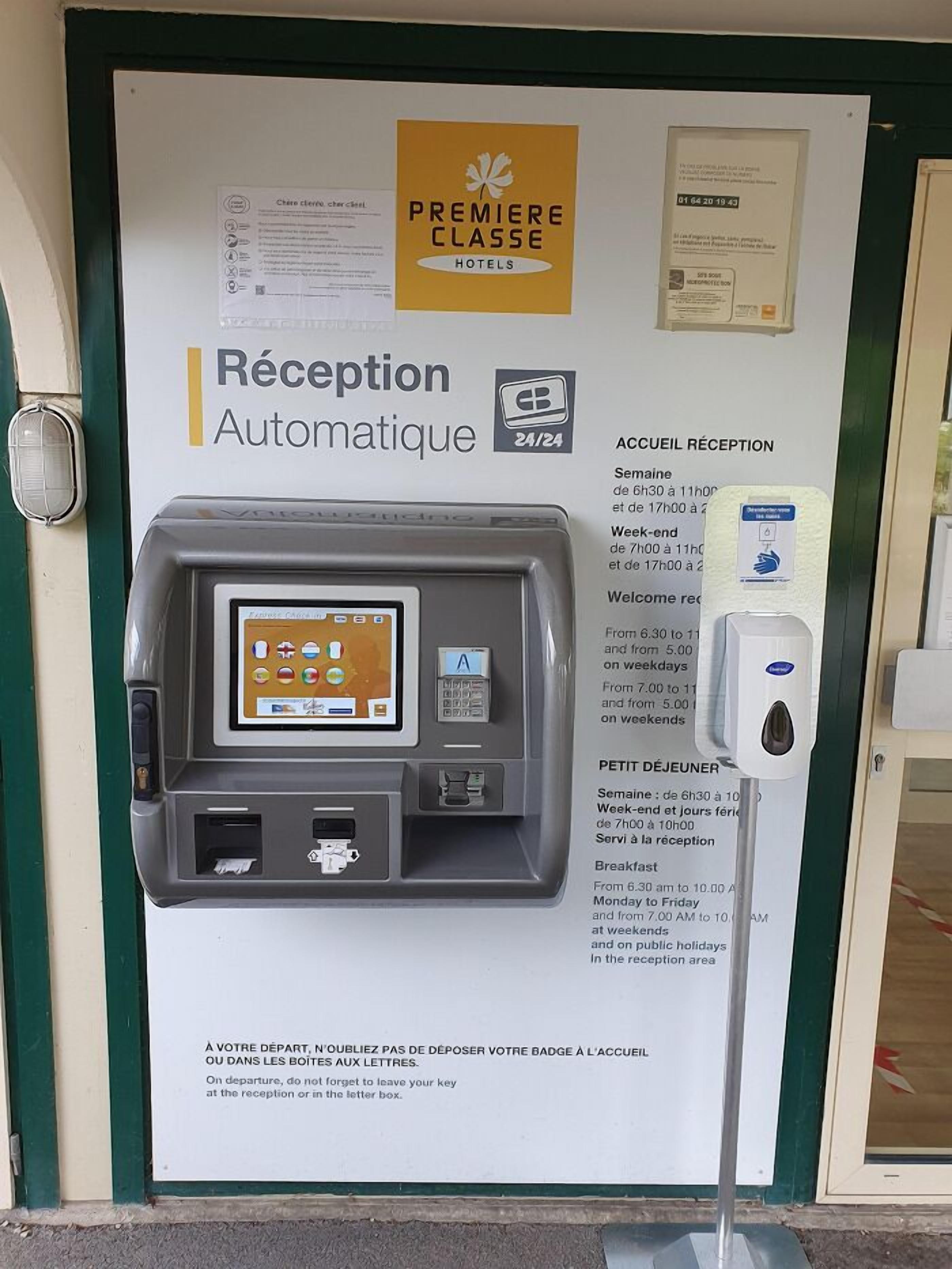 A hotel reception area with an automated reception machine, a key card dispenser, and a sign indicating reception hours.