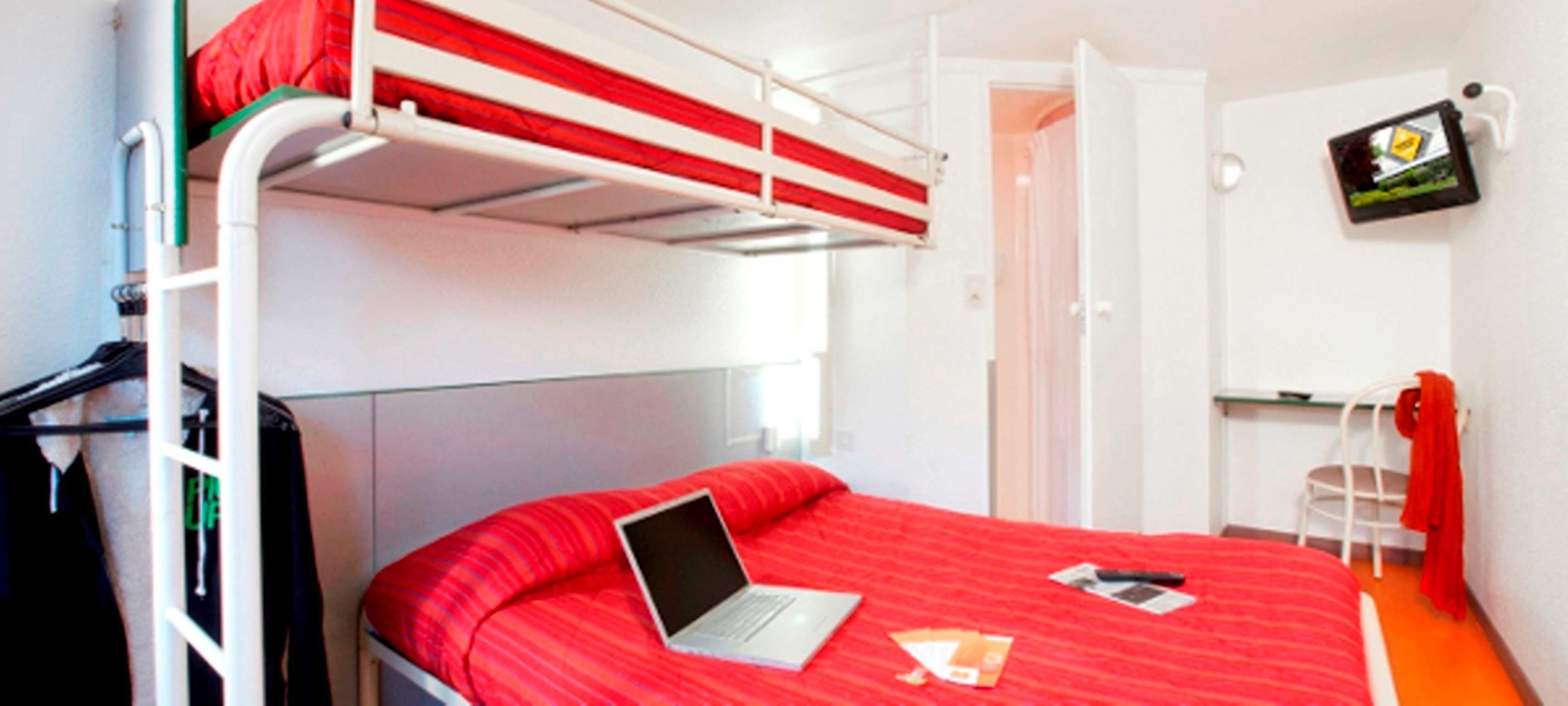 A bunk bed room with a laptop on the lower bed, a small table, and a TV on the wall.