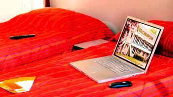 Un portatile su un letto con una coperta rossa, un telecomando e uno smartphone.
