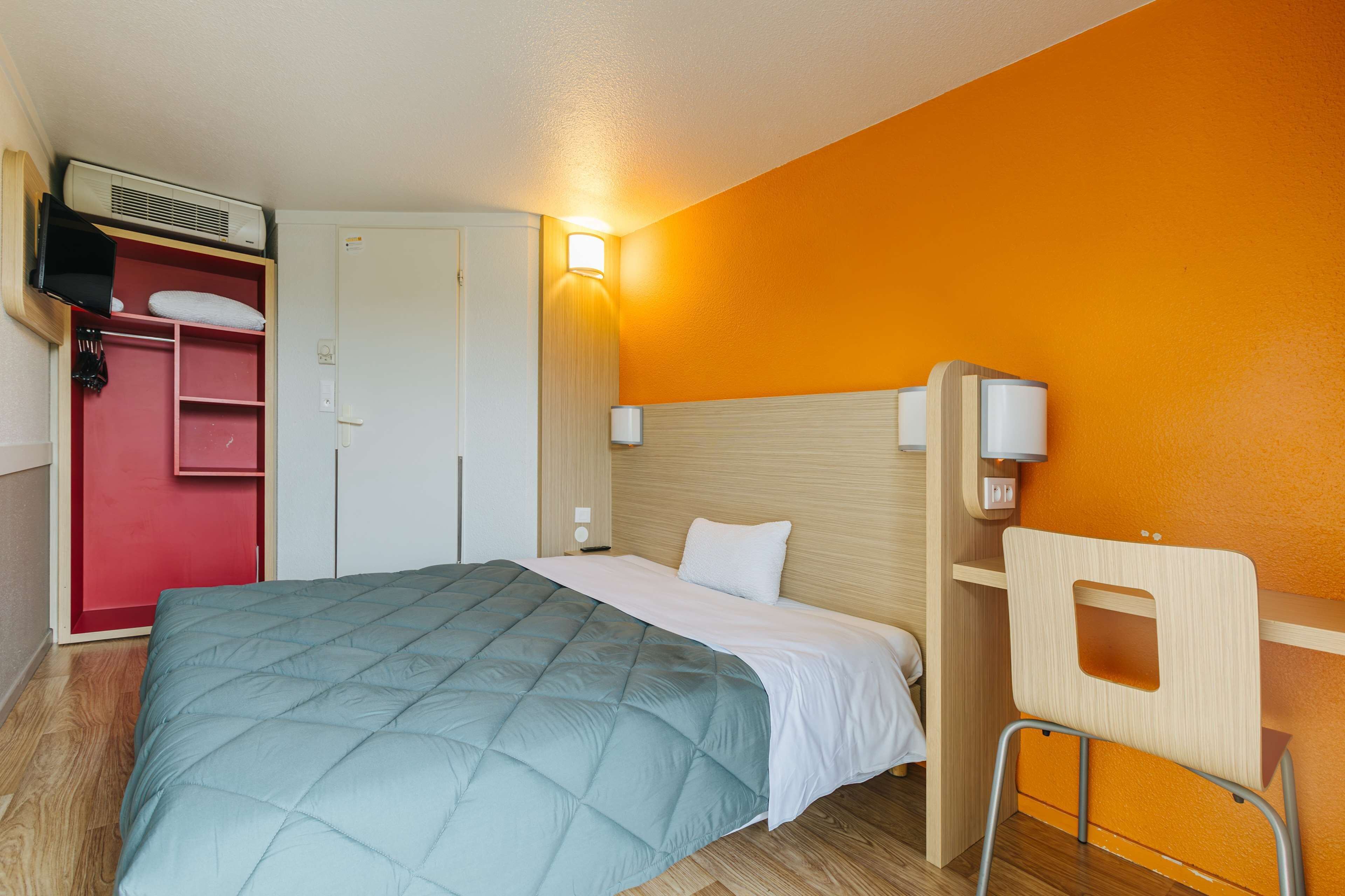 Ein Hotelzimmer mit einem Bett, einem roten Kleiderschrank, einem Schreibtisch mit Stuhl und einer Wandleuchte.