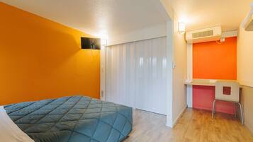 A room with a bed, a desk, a chair, a white wardrobe, and an air conditioning unit.