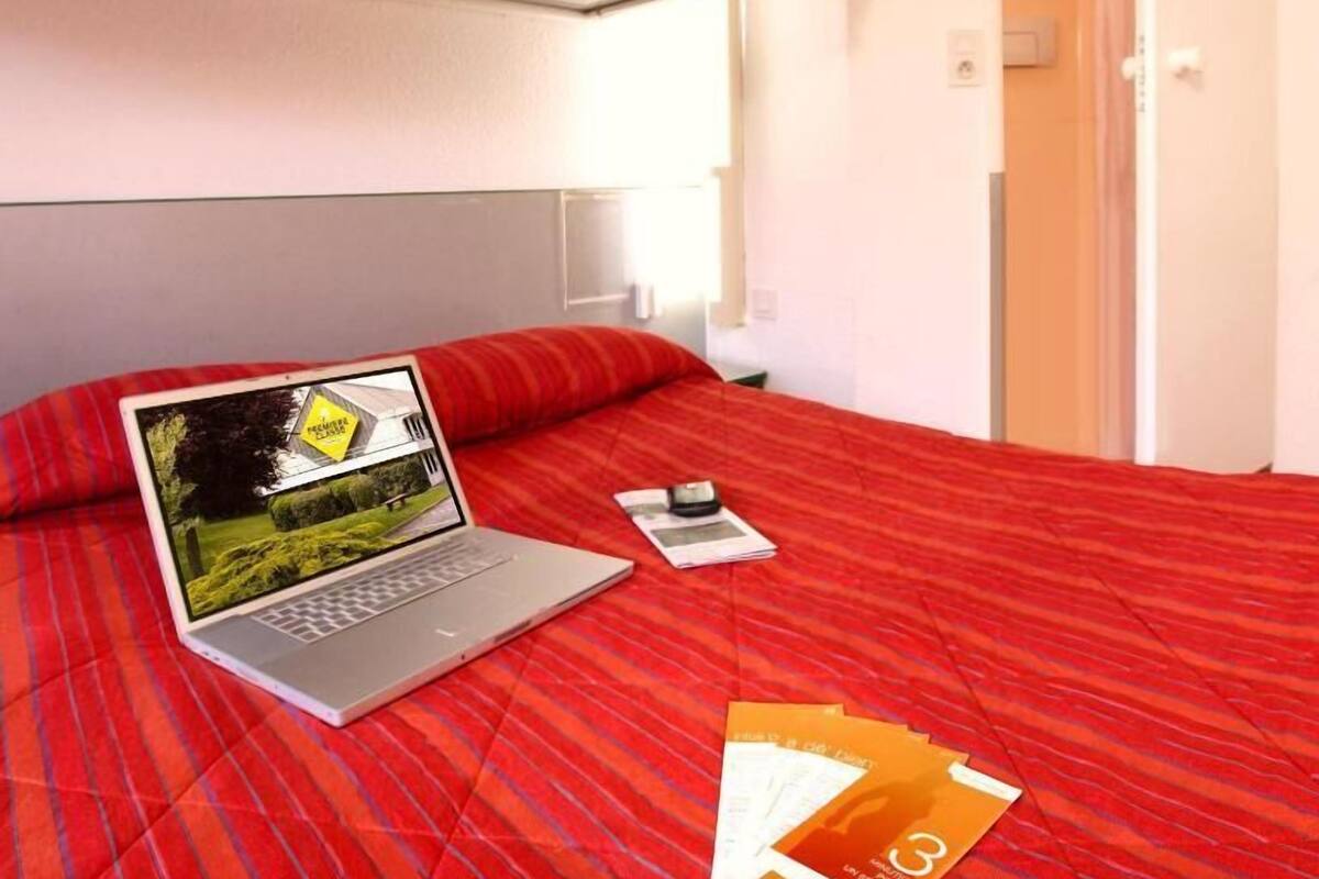 Une chambre d’hôtel avec un lit, un ordinateur portable, un téléphone portable et quelques brochures.