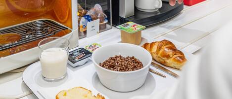 A breakfast setup with a coffee machine, a croissant, a bowl of cereal, and a glass of milk.
