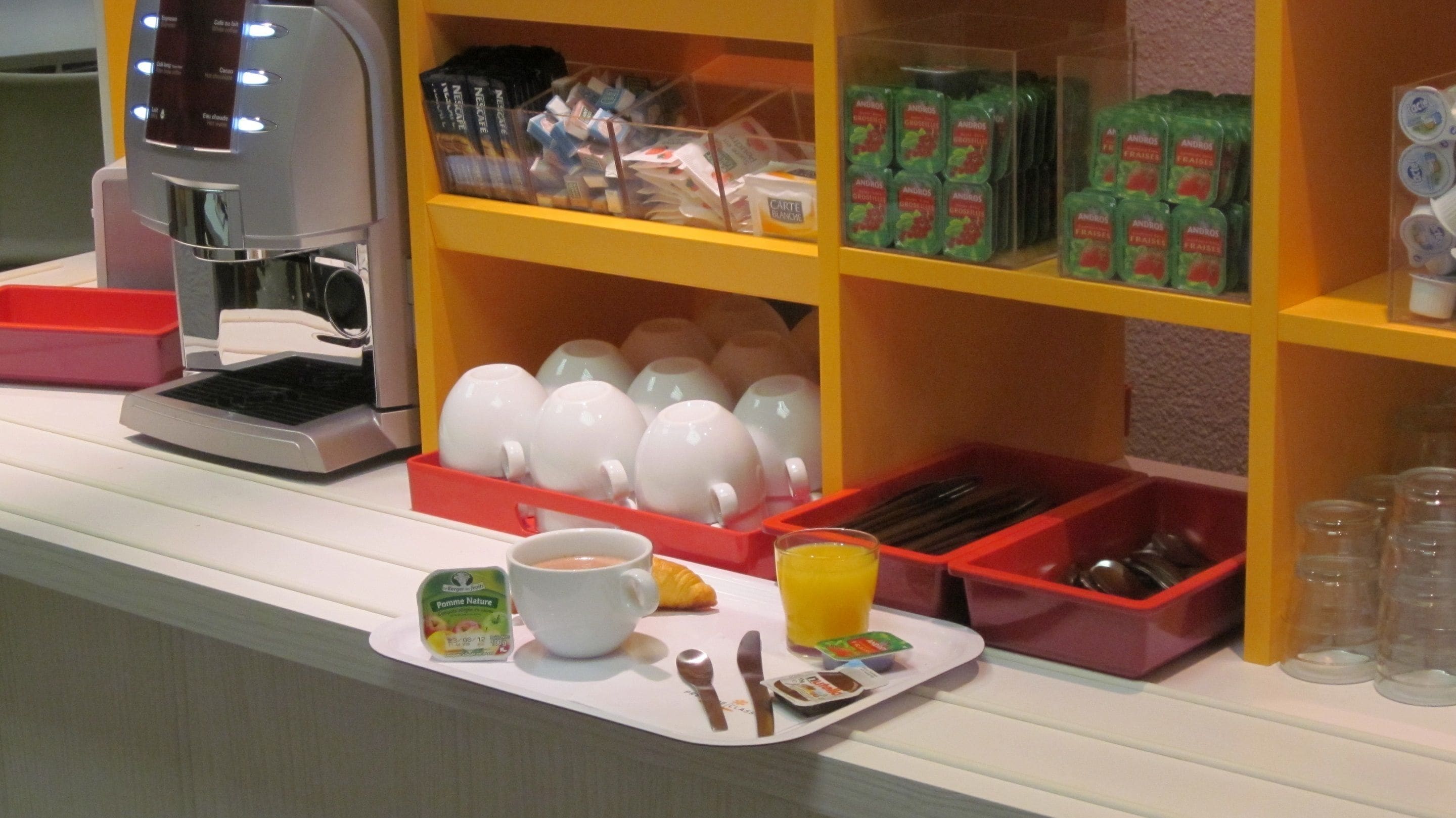Ein Frühstücksbuffet mit verschiedenen Speisen, einer Kaffeemaschine und einer Tablett mit Besteck.
