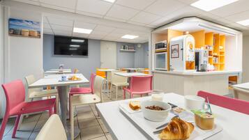 Eine hell erleuchtete Cafeteria mit weißen und rosa Stühlen, Tischen und einer Theke mit einer Kaffeemaschine.