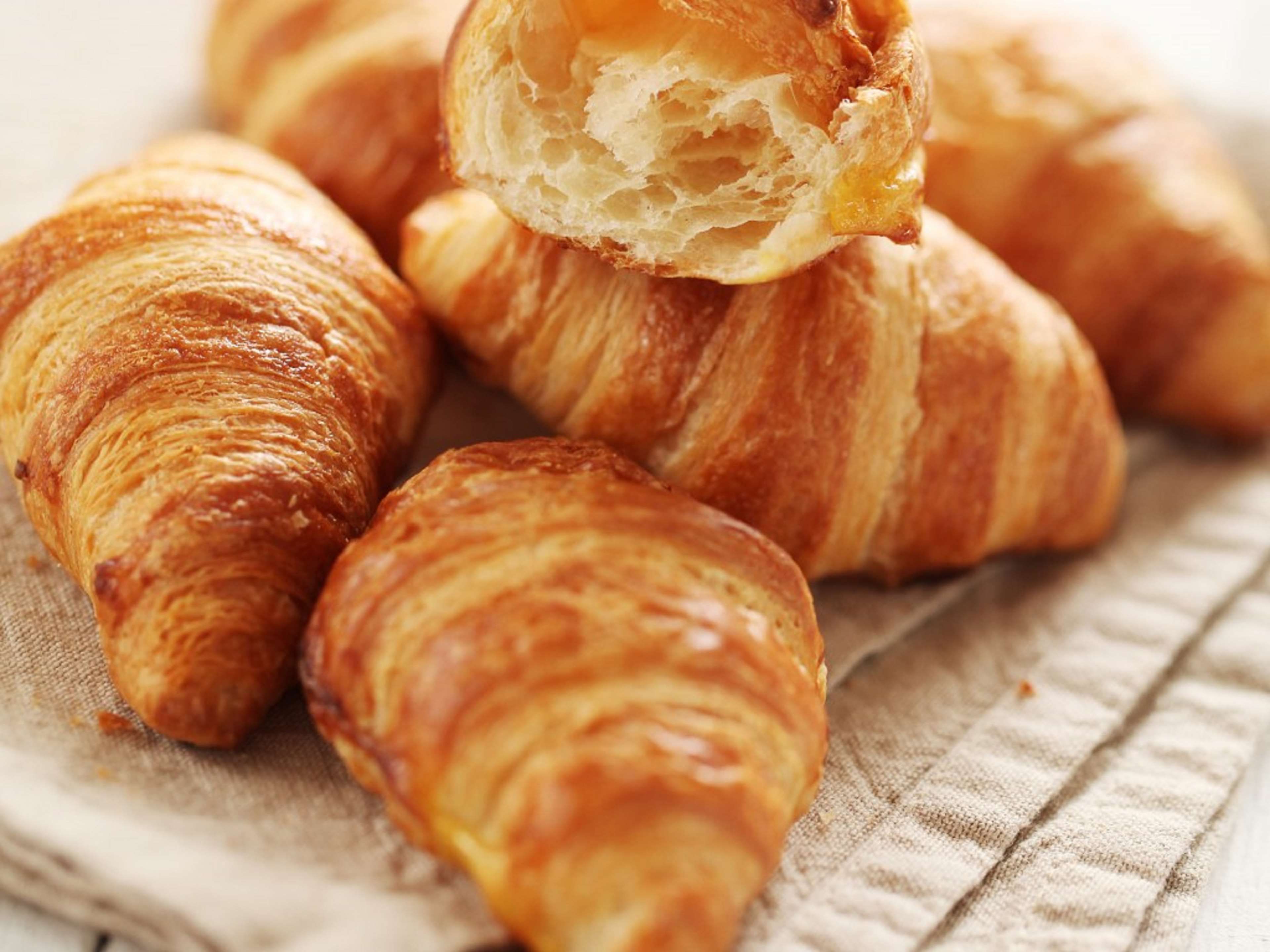 Gros plan sur des croissants, dont l’un est cassé en deux, révélant une mie feuilletée, le tout posé sur une surface en tissu texturé.