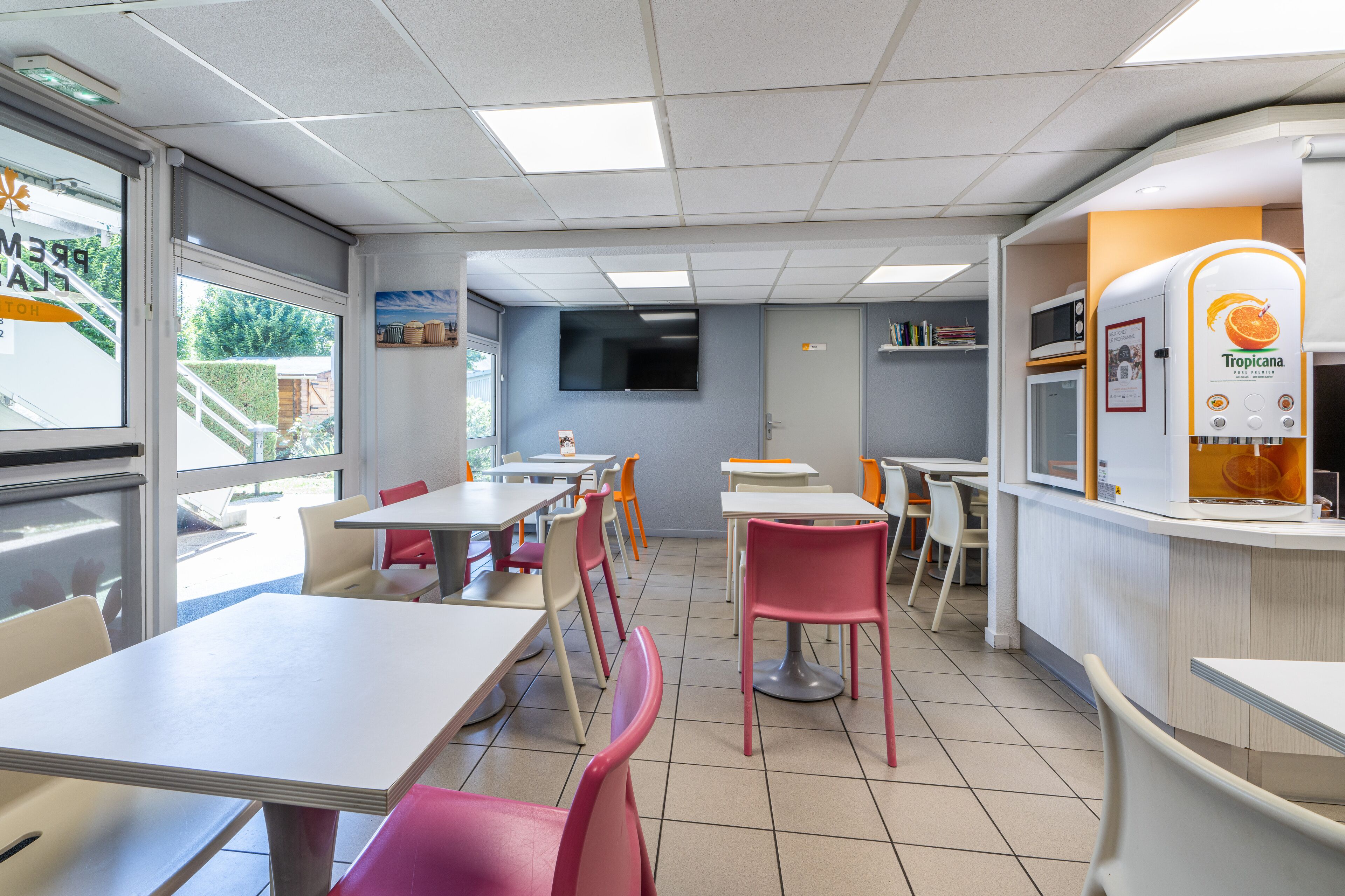 En kantine med borde, stole, et fjernsyn og et køleskab med Tropicana logo.