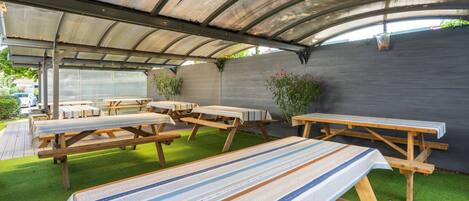 Un patio al aire libre con mesas de picnic y una zona de estar cubierta.