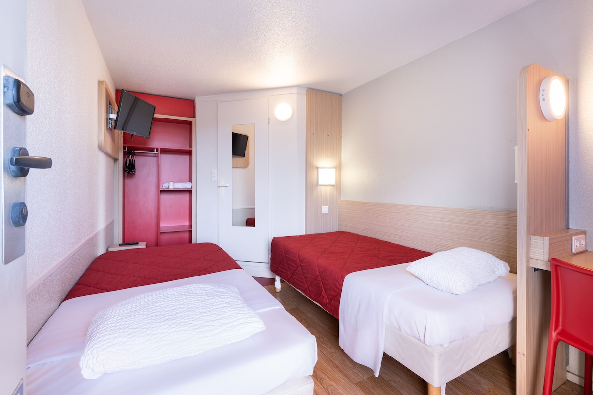 A hotel room with two beds, a TV, a mirror, and a red chair.