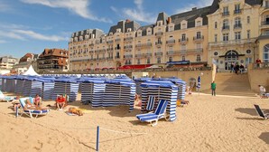 Een strand met rijen gestreepte strandparasols en ligstoelen, een hotel met balkons en een heldere lucht.