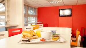 A breakfast tray with croissants, orange juice, and yogurt on a white table in a room with red walls and a television mounted on the wall. - Unisotel Tours Nord (Parcay-Meslay)