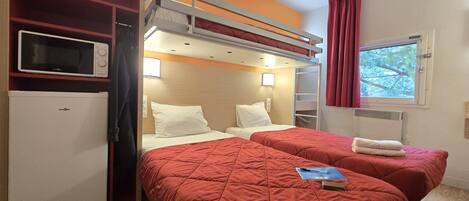 A room with two beds, a microwave, a mini-fridge, a window with curtains, and a shelf with a TV.