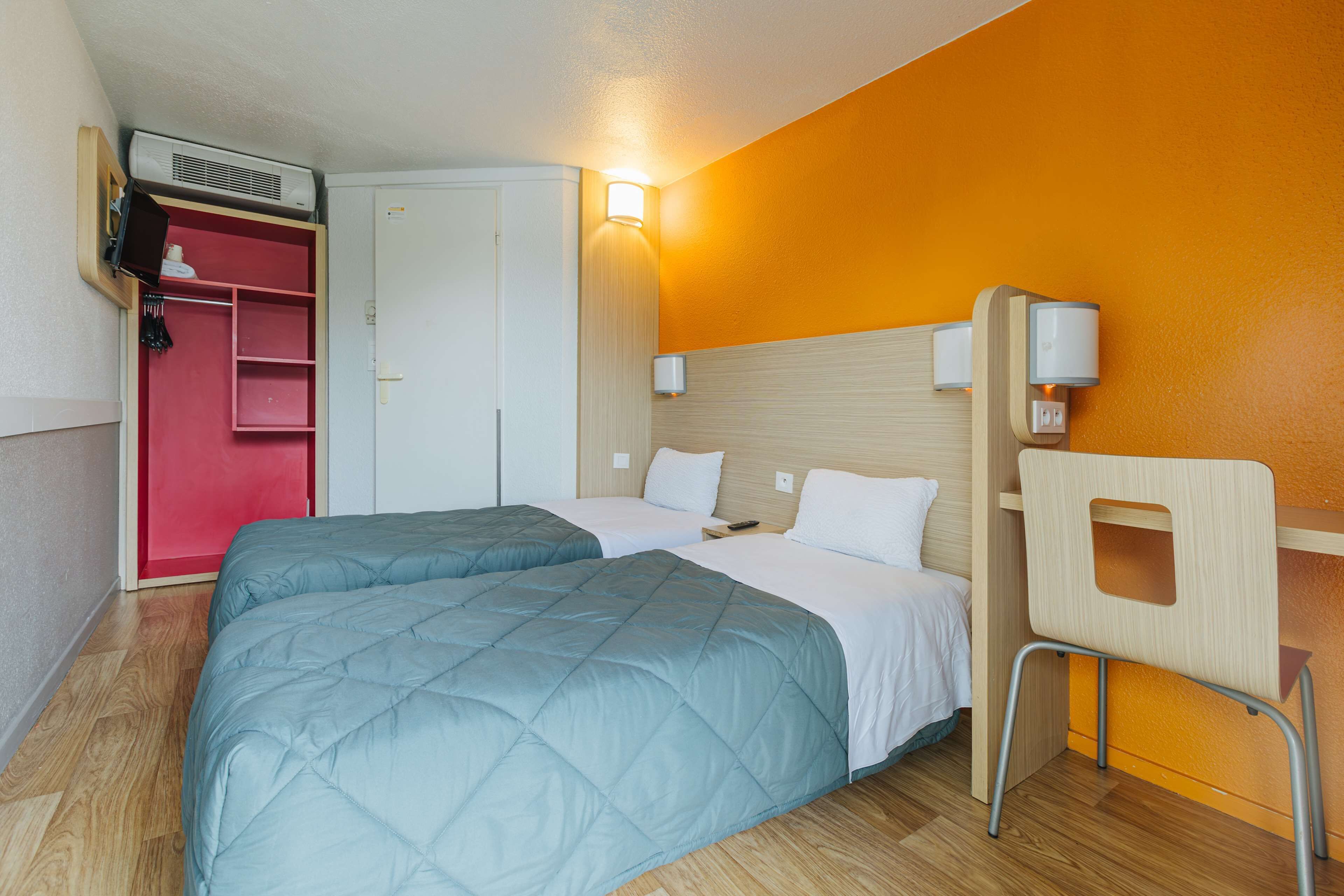 Quarto de hotel com duas camas, um guarda-roupa, uma escrivaninha e uma cadeira.