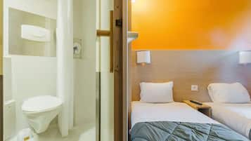 Camera d'albergo con una testiera in legno, due letti con biancheria bianca, un comodino con un telecomando e un water bianco con bidet.