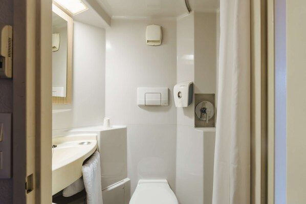 Un baño con inodoro, lavabo y espejo. Hay una toalla colgada en la pared y un dispensador de jabón.
