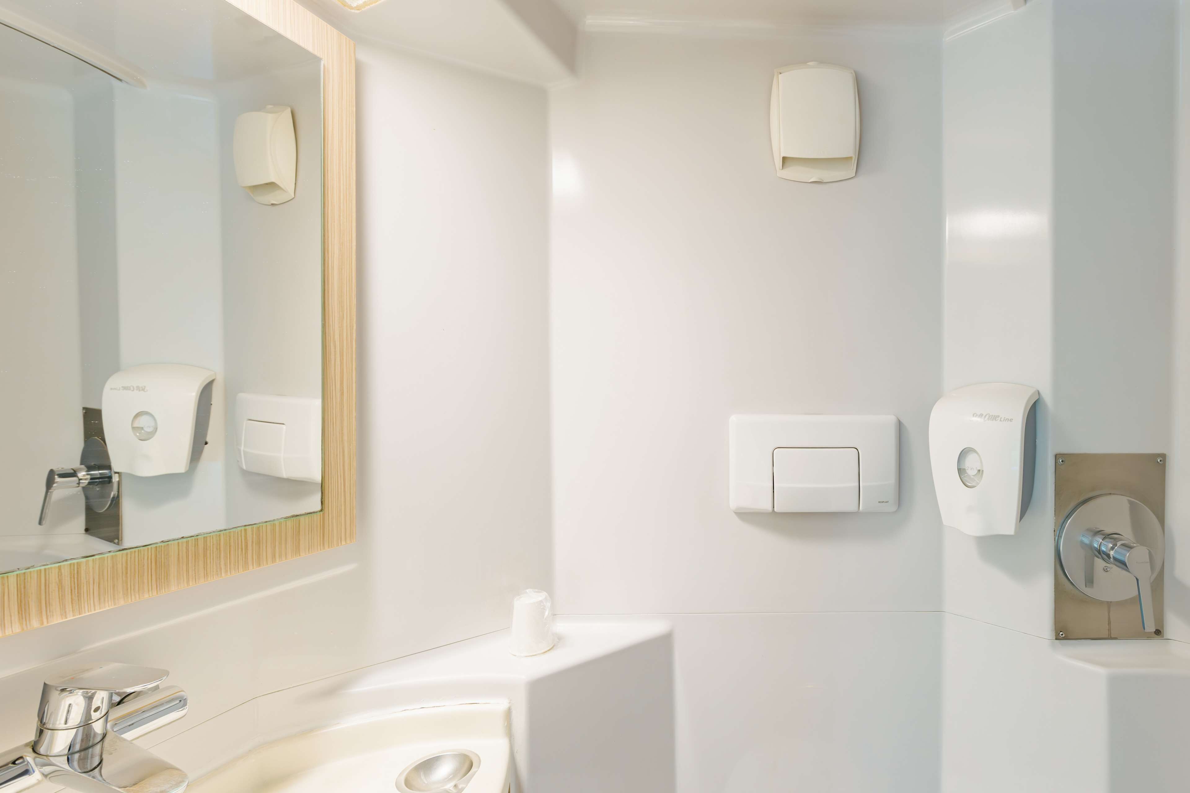 Une salle de bain moderne avec un grand miroir, un lavabo et deux sèche-mains fixés au mur.