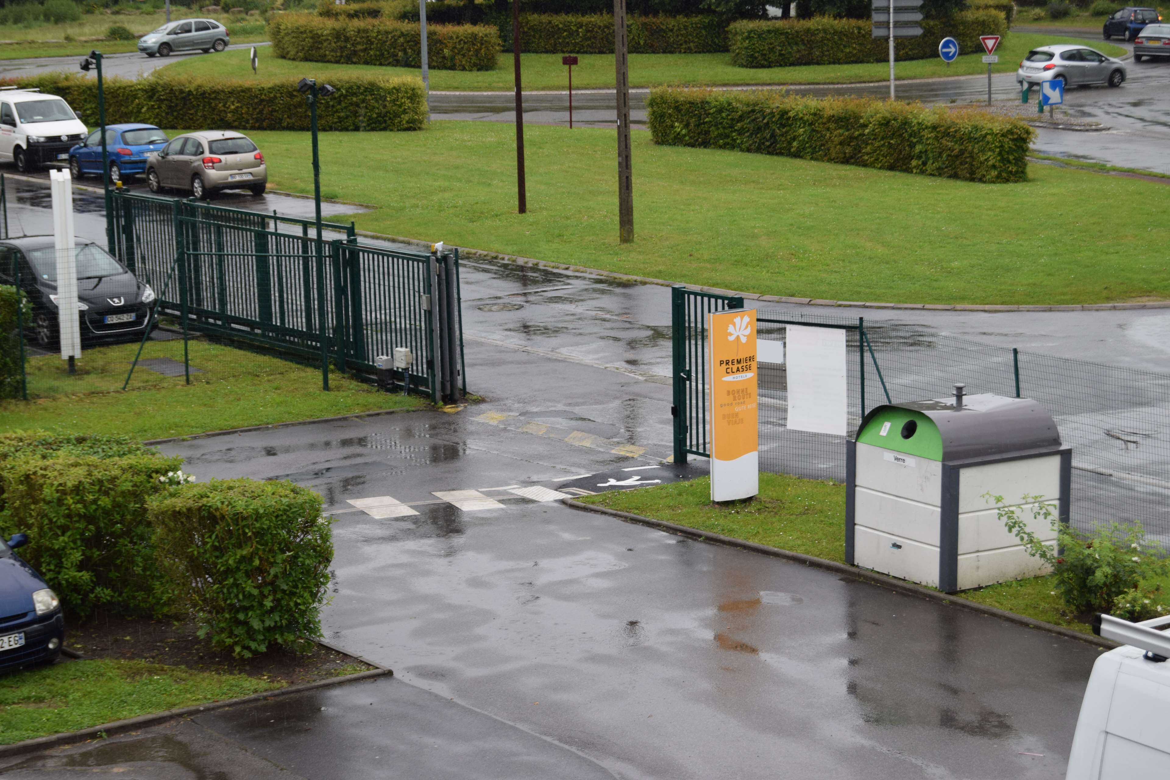 Une entrée fermée par un portail donnant sur une propriété, avec une clôture verte, un panneau indicateur et une petite poubelle.