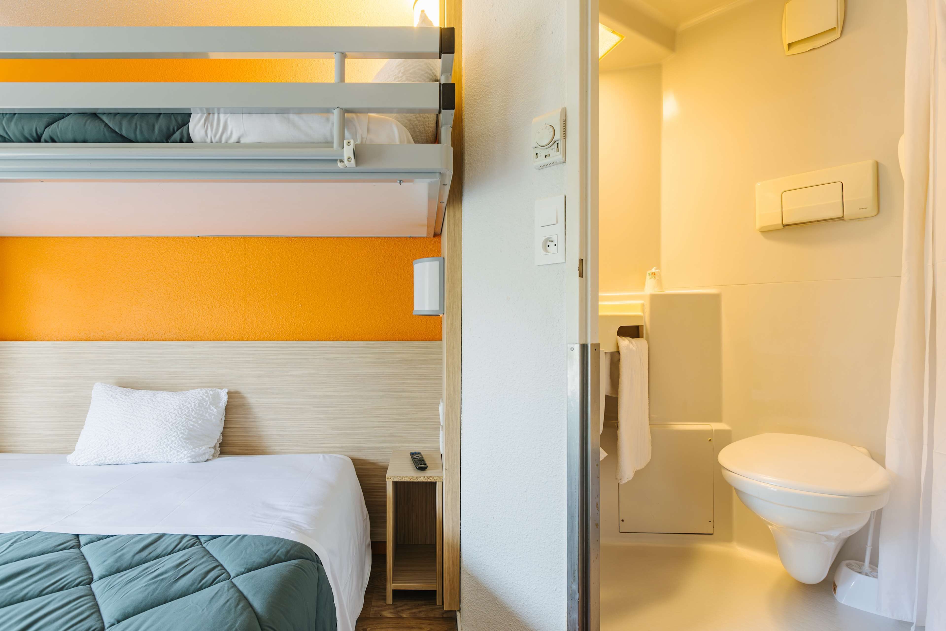 Habitación de hotel con literas, una mesita de noche pequeña, un inodoro blanco y una zona de ducha.