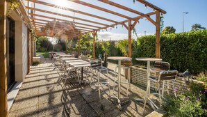 An outdoor patio with tables and chairs, a pergola with string lights, and a garden area with plants and flowers. - Premiere Classe Laon (Laon)