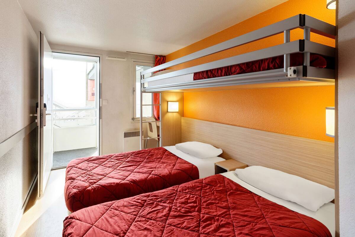 A hotel room with two beds, a bunk bed, a desk, and a chair.