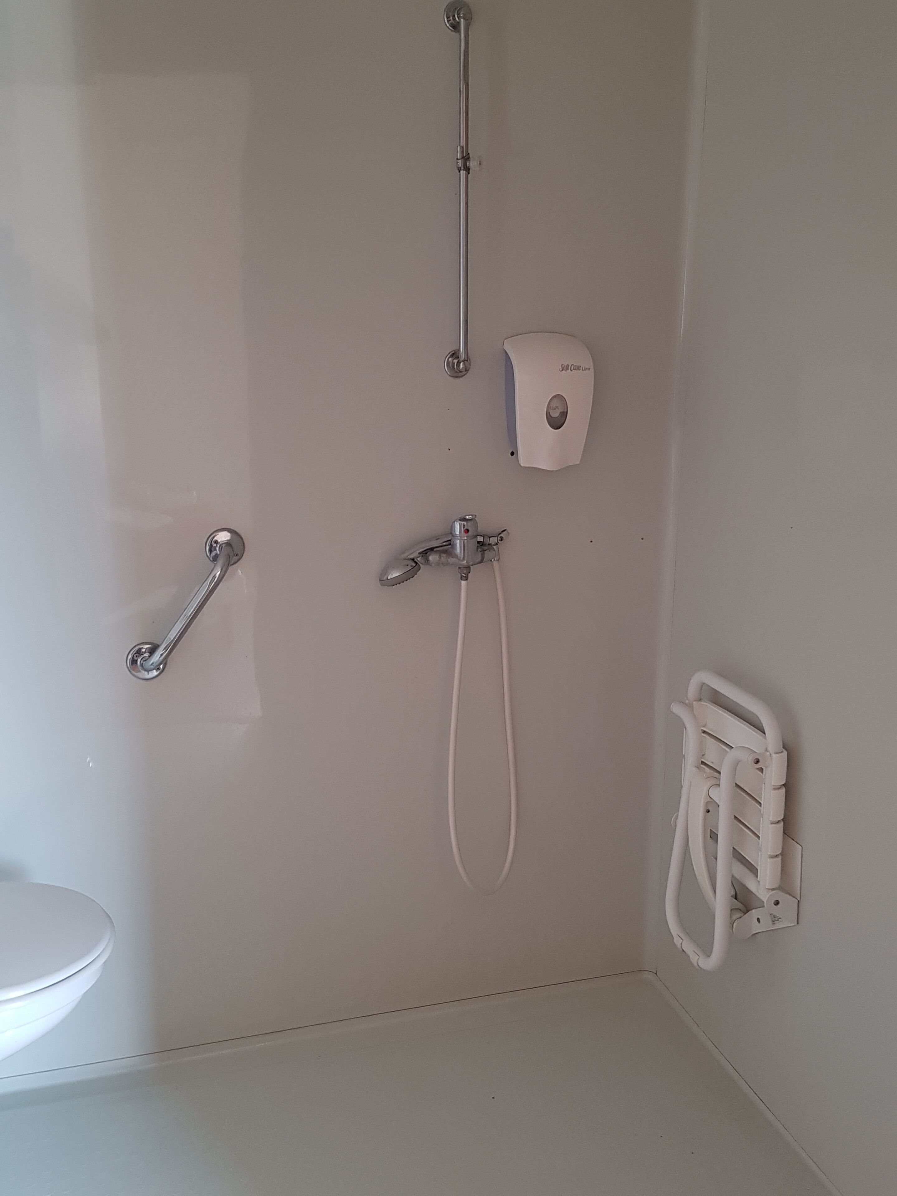 A bathroom with a toilet, a shower, and a hand dryer.