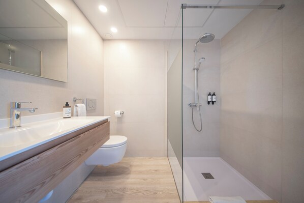 A modern bathroom with a glass-enclosed shower, a wooden vanity, and a white toilet.