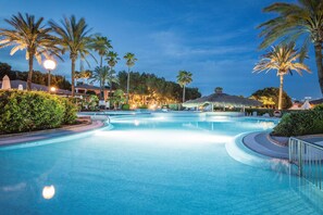 A large, clear swimming pool with palm trees and a thatched-roof structure in the background. - Blau Colònia Sant Jordi (Ses Salines)