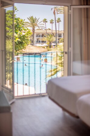 Habitación de hotel con vista a una piscina y palmeras.