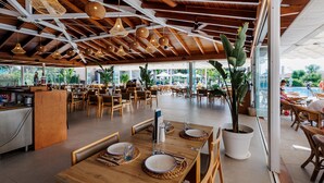 A spacious dining area with wooden tables and chairs, large windows, and hanging wicker light fixtures. - Blau Colònia Sant Jordi (Ses Salines)