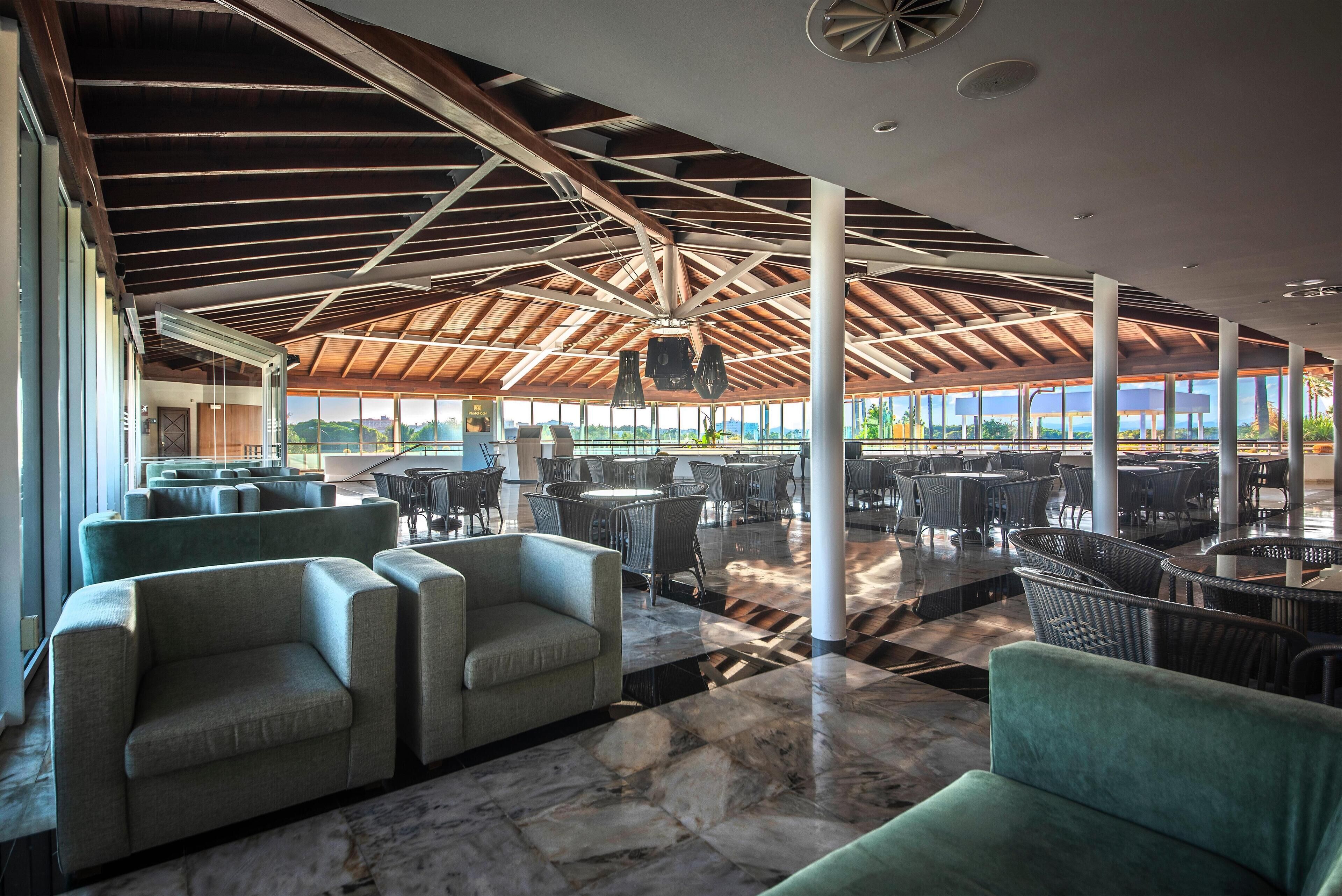 A spacious indoor area with multiple seating arrangements, including sofas and chairs, under a high ceiling with exposed beams.