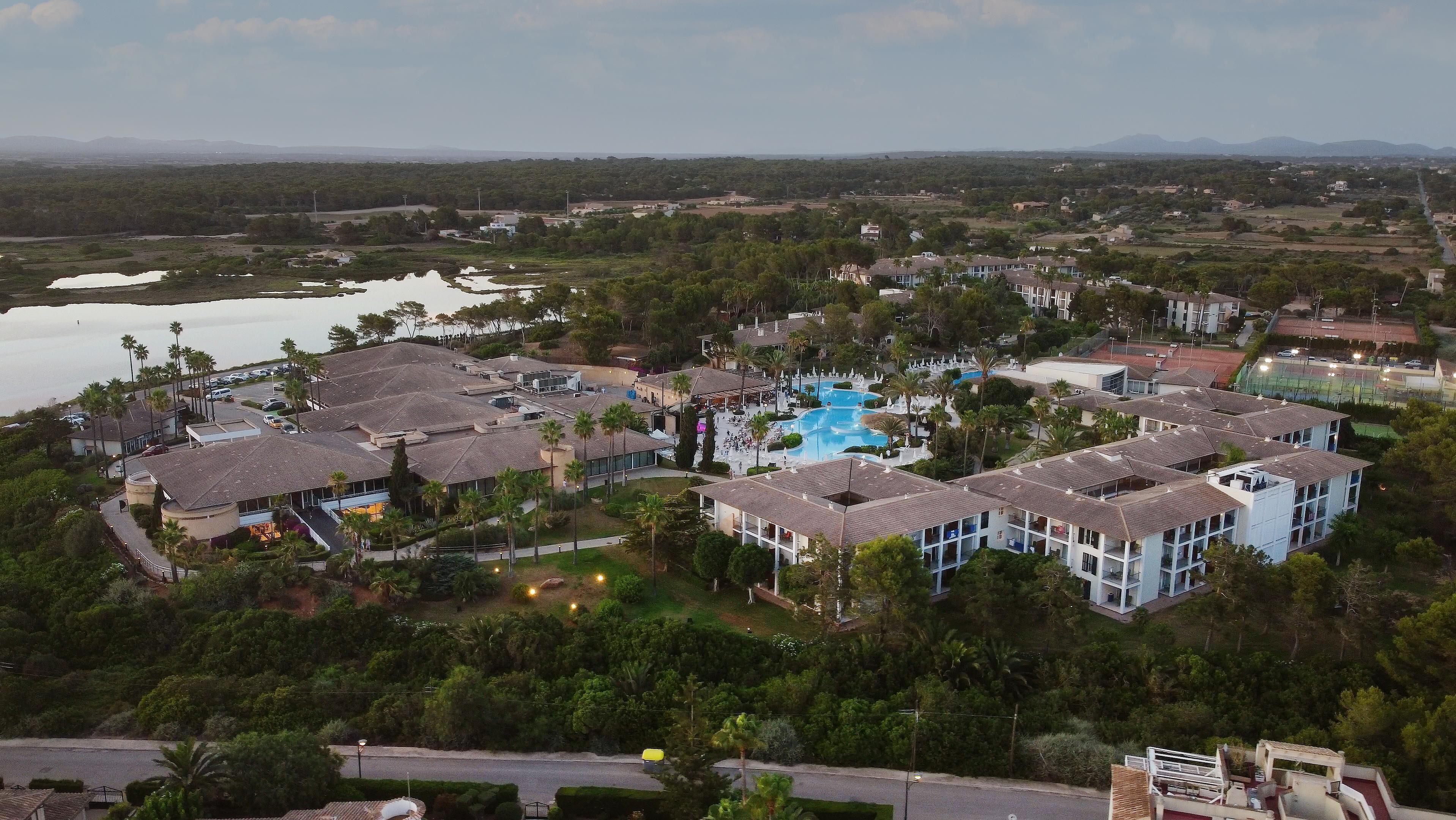 An aerial view of a resort with multiple buildings, a swimming pool, and surrounding greenery.