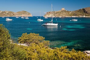 A coastal scene with boats, clear water, and a castle on a hill. - Blau Colònia Sant Jordi (Ses Salines)